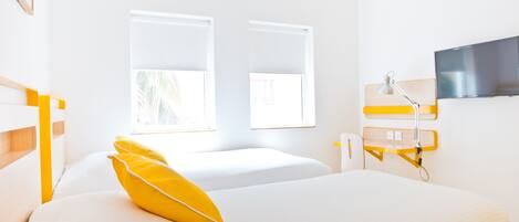 Habitación de hotel con dos camas, televisión y ventana con vistas a palmeras.