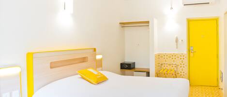 Una habitación de hotel con una cama, mesita de noche, lámpara y una puerta amarilla.