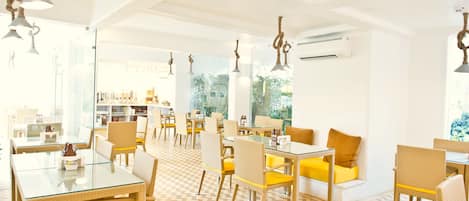 A bright, modern dining area with glass tables and wicker chairs, featuring a geometric patterned floor and natural light from large windows.