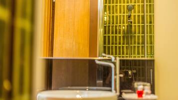 Un baño con lavamanos blanco, espejo y ducha con azulejos verdes.