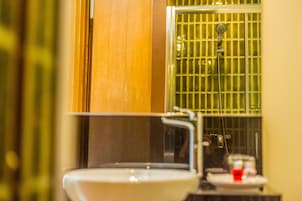 A bathroom with a white sink, a mirror, and a shower with green tiles.