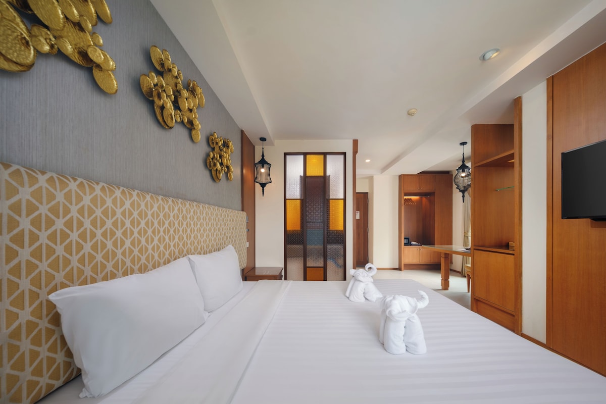 A hotel room with a large bed, a wooden wardrobe, a television, and a decorative wall piece.