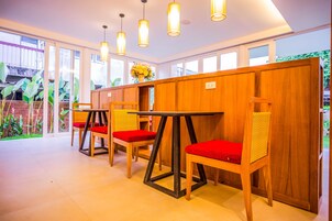 A dining area with wooden tables and chairs, a brick wall, and a large window with a view of greenery.