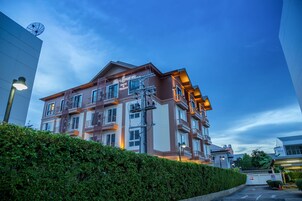 A multi-story hotel with balconies, a satellite dish, and a well-maintained hedge in front.