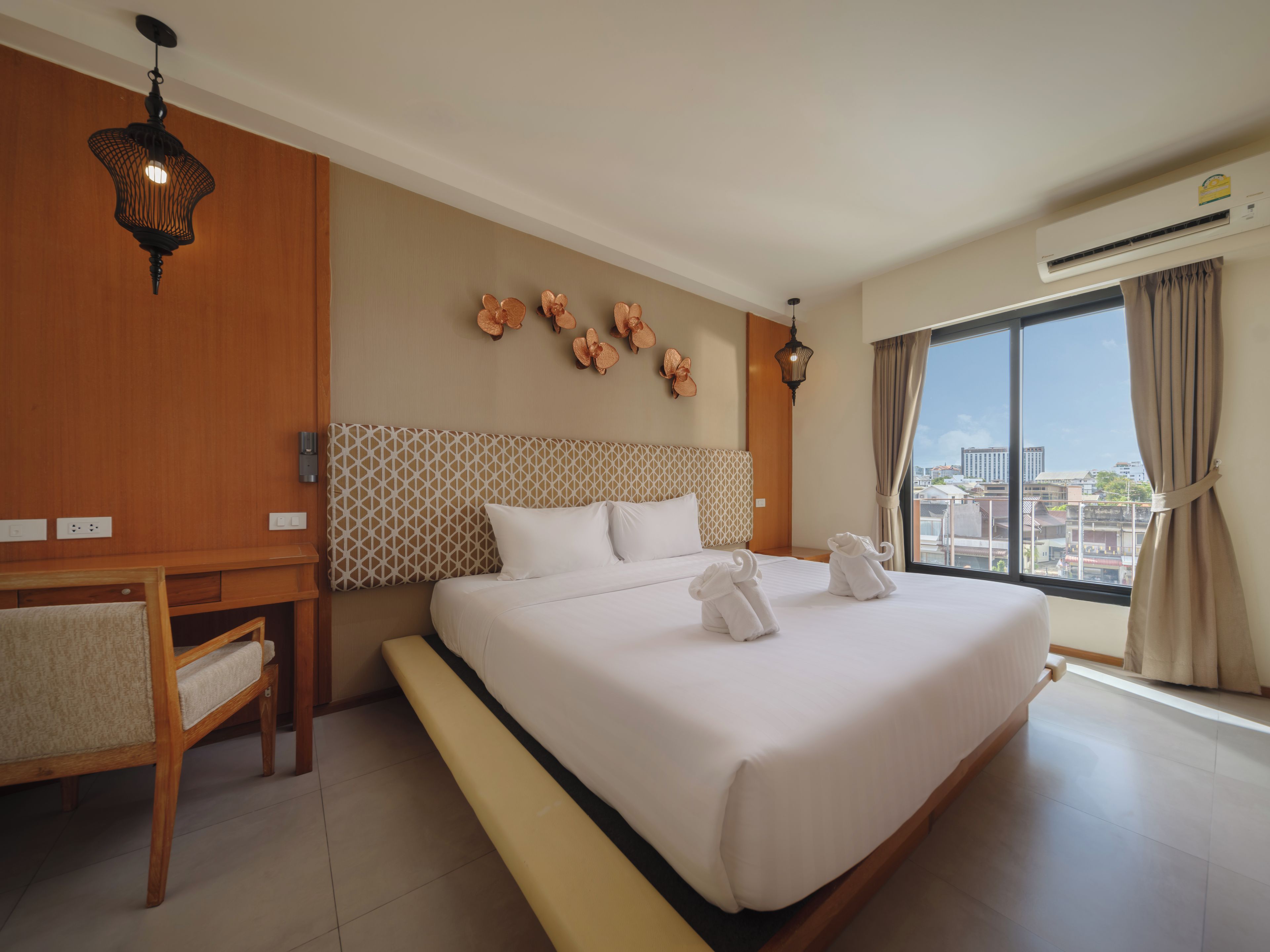 Habitación de hotel con una cama grande, un escritorio, una silla, aire acondicionado de pared y vistas a la ciudad a través de la ventana.