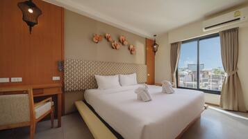 Habitación de hotel con una cama grande, un escritorio, una silla, aire acondicionado de pared y vistas a la ciudad a través de la ventana.