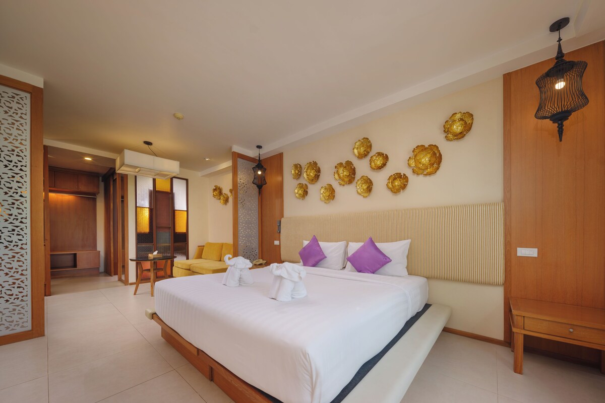 A hotel room with a large bed, a wooden headboard, a sofa, and a decorative wall with golden accents.