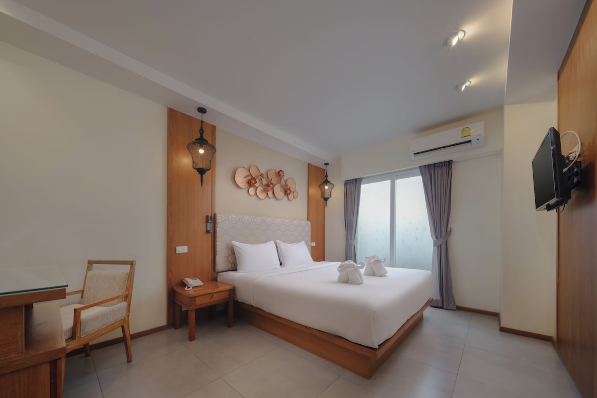 A hotel room with a bed, bedside table, chair, and a TV mounted on the wall.