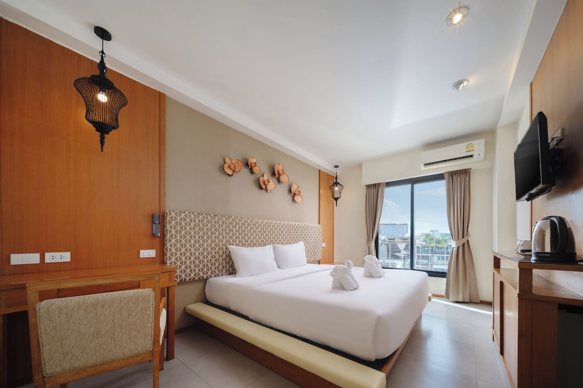 A hotel room with a large bed, a desk, a chair, a television, and a window with a view of the city.