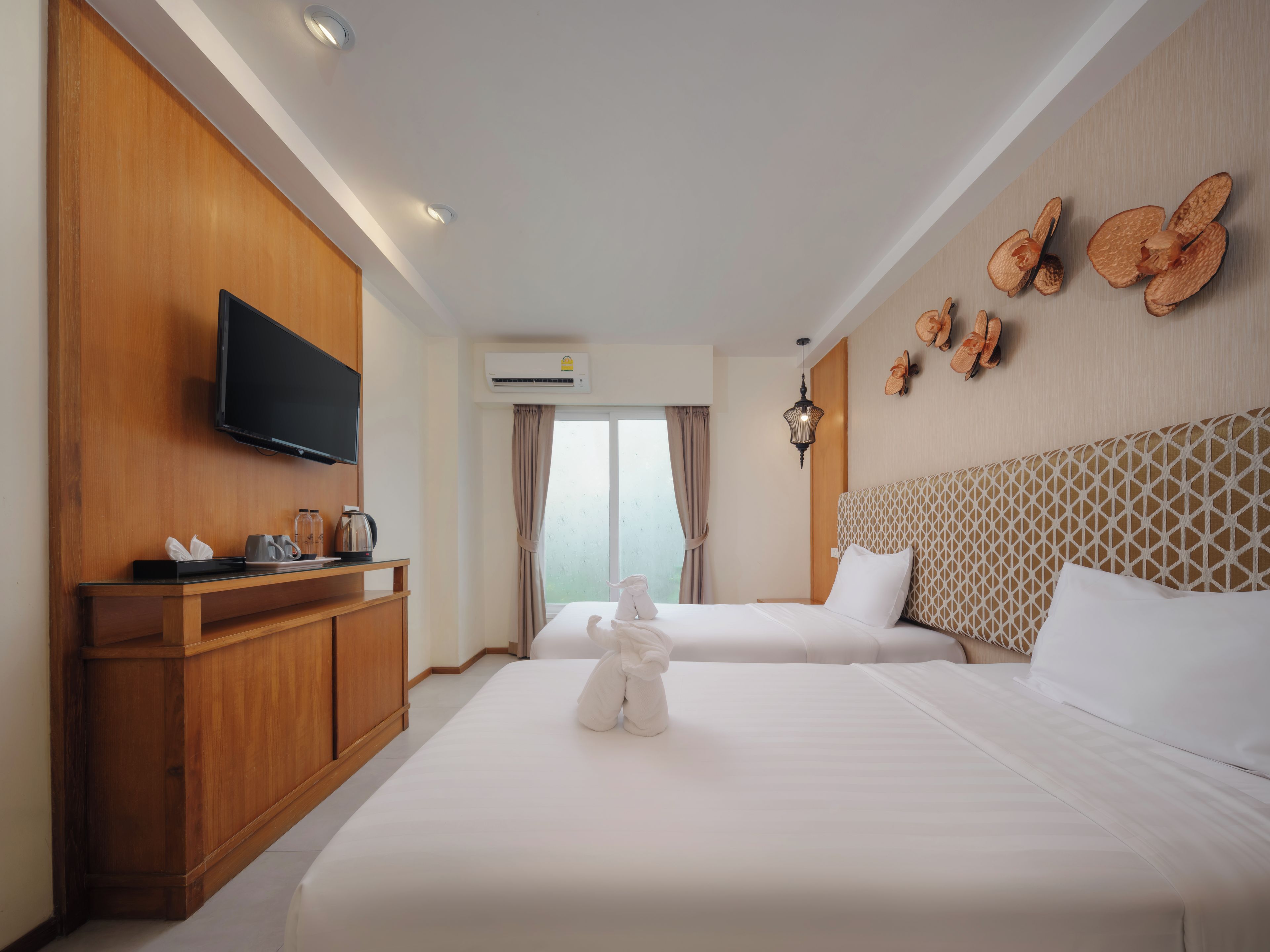 A hotel room with two beds, a TV, a minibar, and a window with curtains.