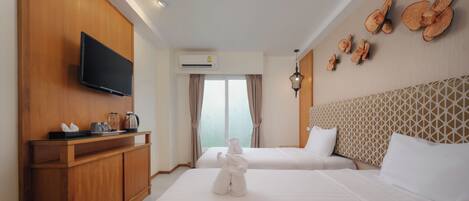 A hotel room with two beds, a TV, a minibar, and a window with curtains.