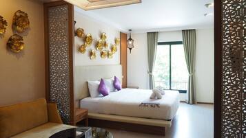 A hotel room with a bed, a sofa, a small table, decorative wall art, and a window with curtains.