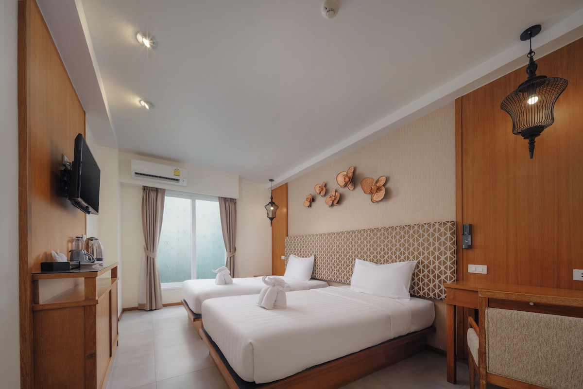 A hotel room with a large bed, a TV, a desk, and a window with curtains.