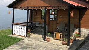 Una cabaña de madera con techo rojo, un porche cubierto con sillas y vistas a las montañas.