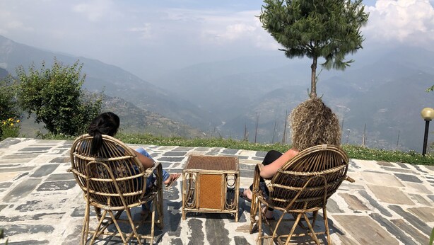 Dos sillas de mimbre mirando a una mesa con una radio, con vista a un paisaje montañoso.