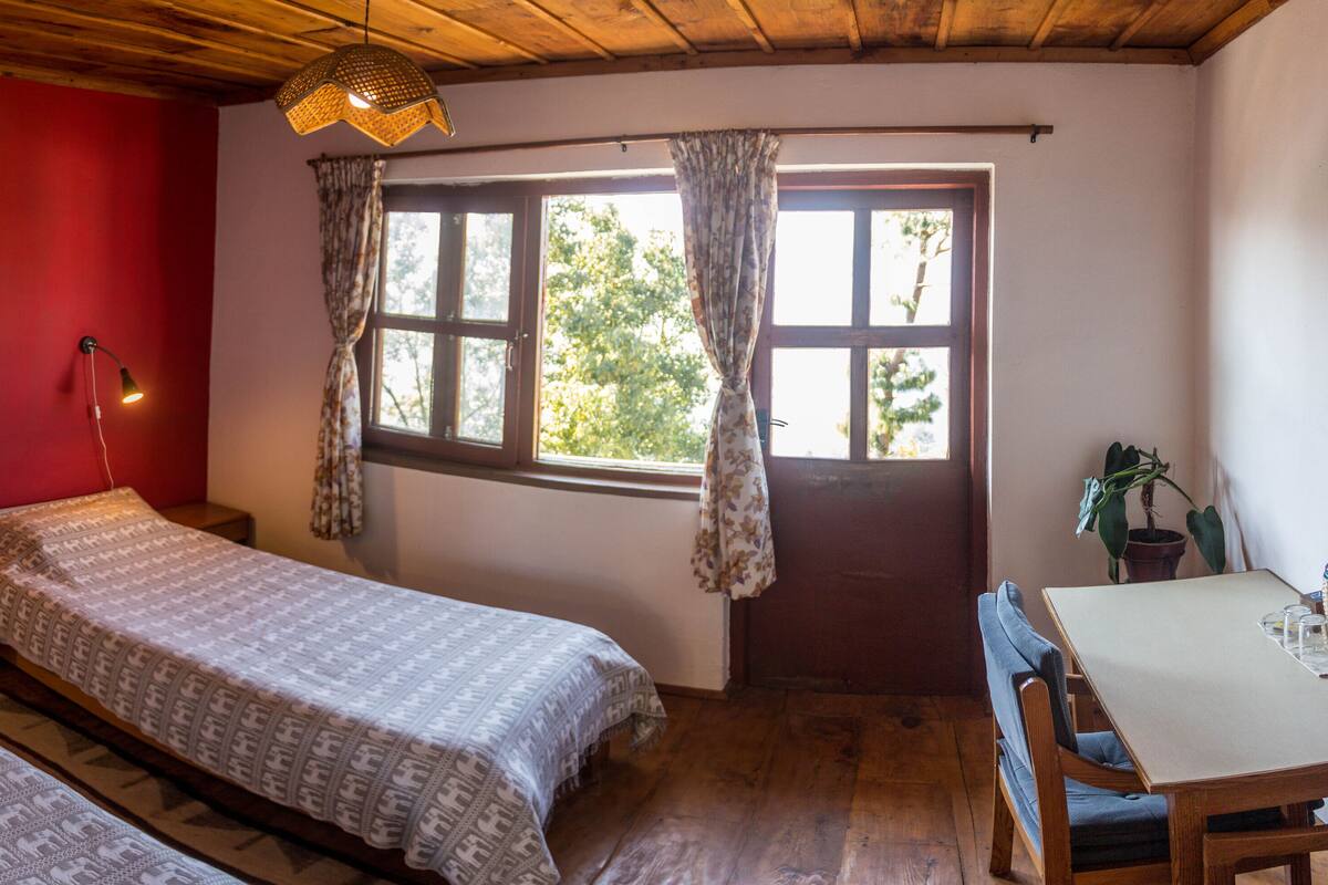 Una habitación con dos camas, una mesa y un ventanal con cortinas.