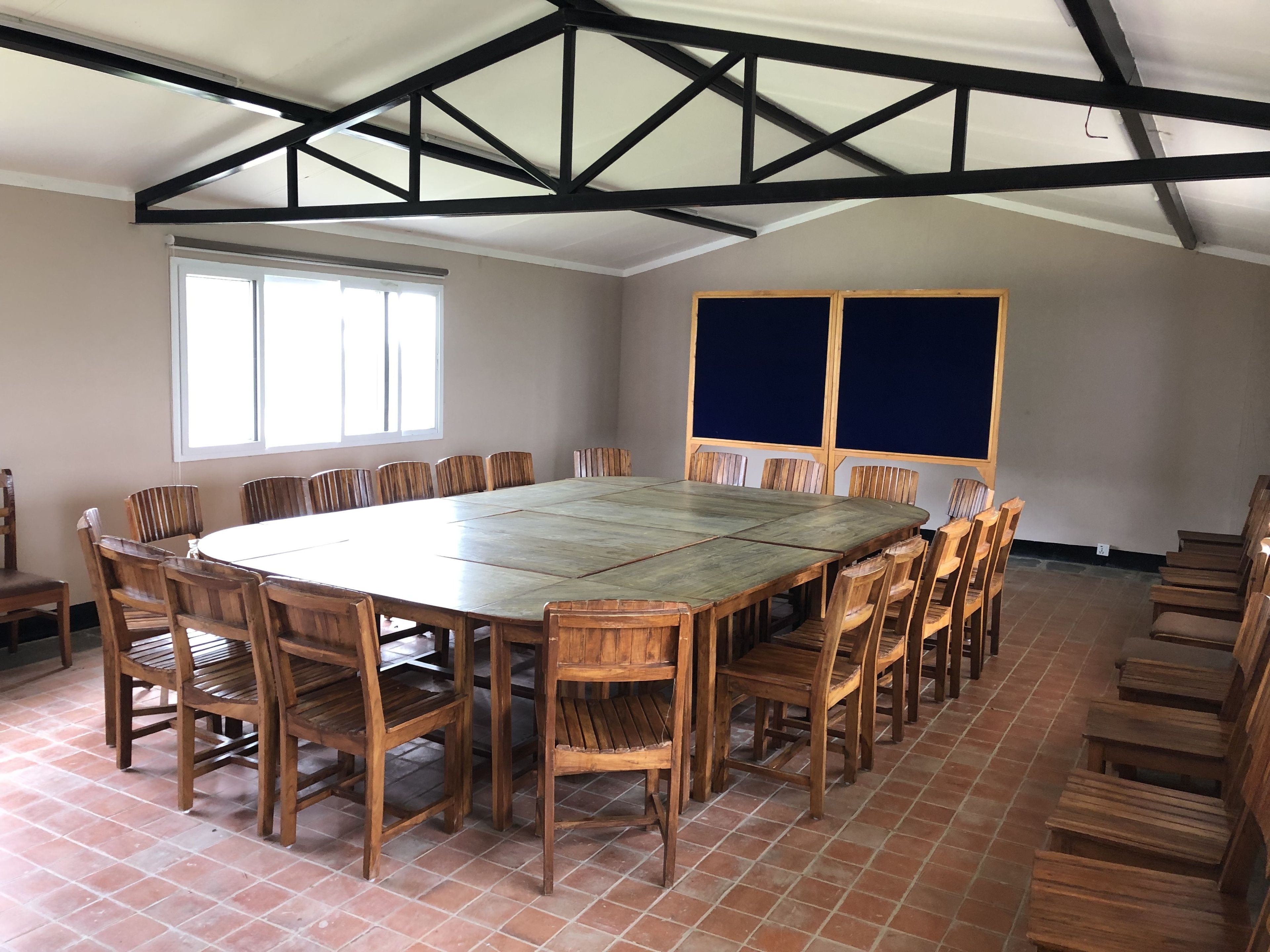 Ein großer, rechteckiger Holztisch, umgeben von Holzstühlen, in einem Raum mit hoher Decke und freiliegenden Balken.