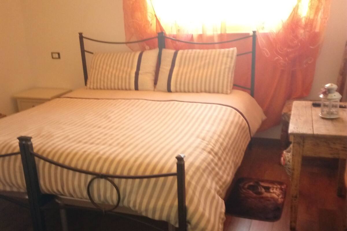 Une chambre à coucher avec un lit, un plancher en bois, des rideaux et une petite table avec une lampe.