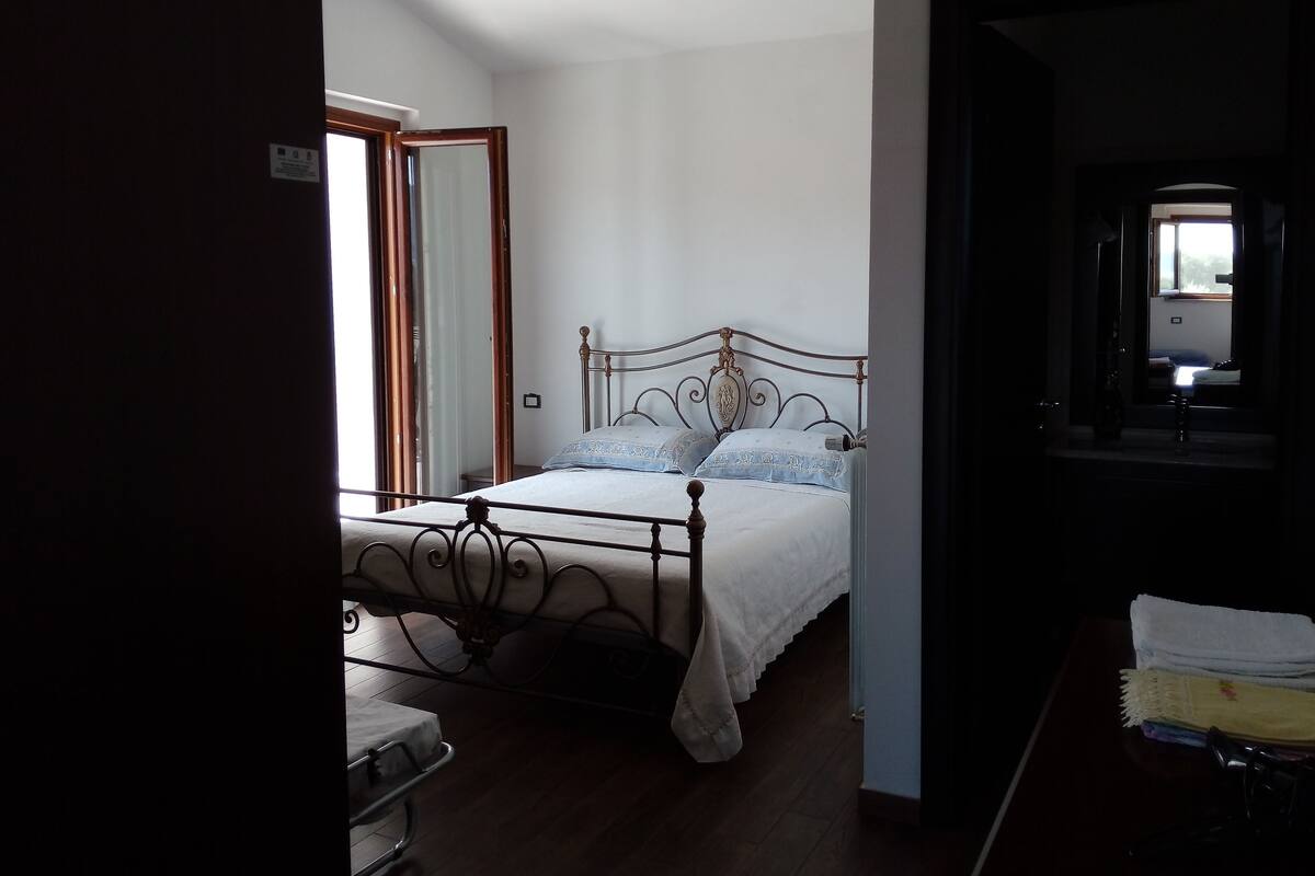 Une chambre à coucher avec un lit à ossature métallique, un plancher en bois et une fenêtre donnant sur l’extérieur.