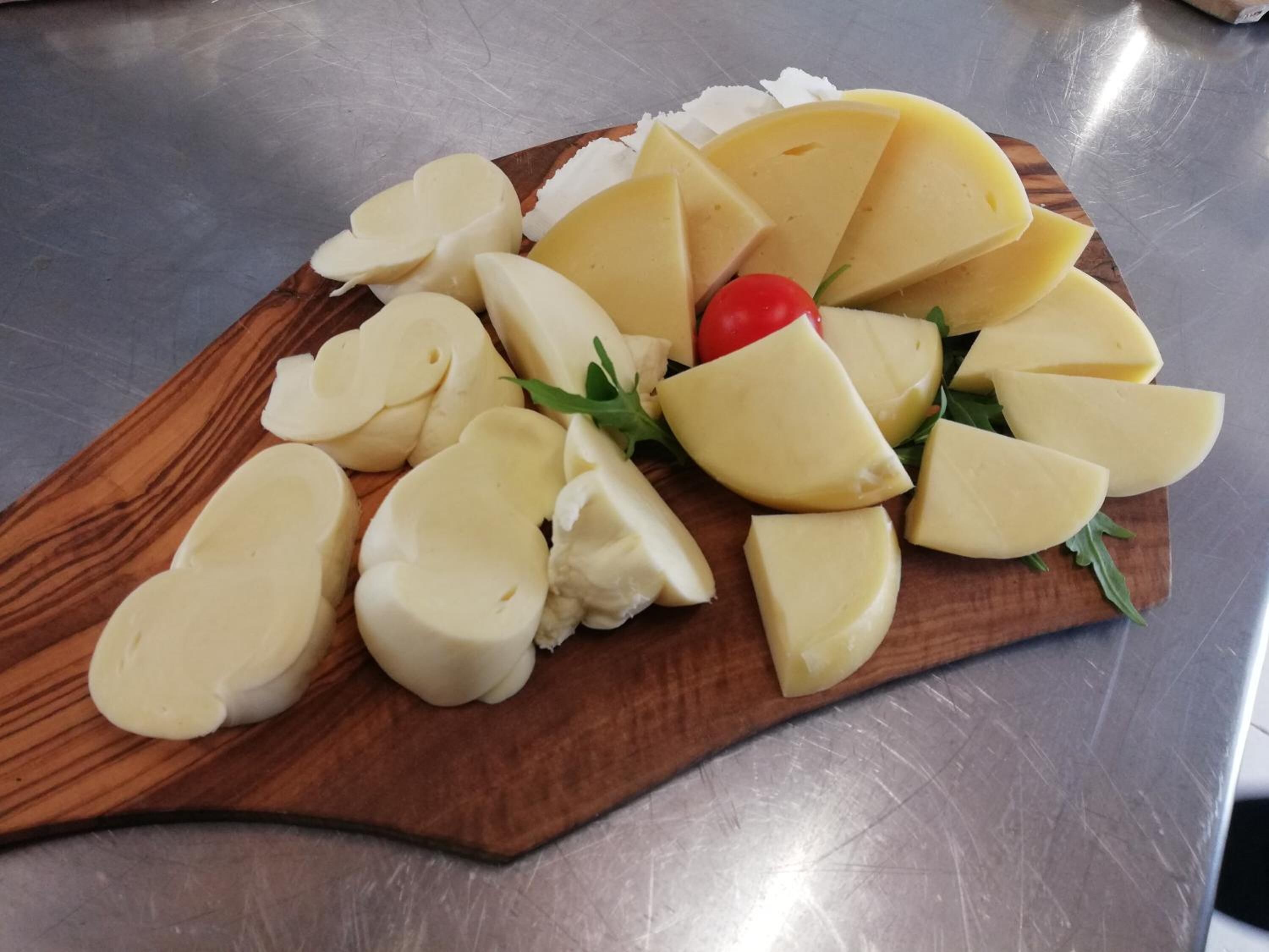 Una tabla de madera con varios quesos y un tomate cherry sobre una superficie metálica.