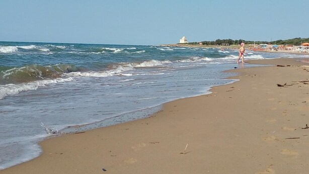 Een strand met golven, een vuurtoren en iemand die loopt.