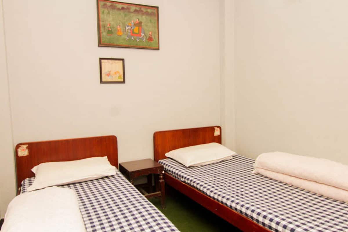 A room with two single beds, a small wooden nightstand, and a framed picture on the wall.
