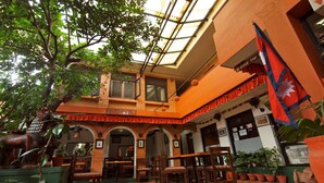 A traditional building with a covered patio, wooden furniture, and potted plants. - Cafe de Patan (Lalitpur)