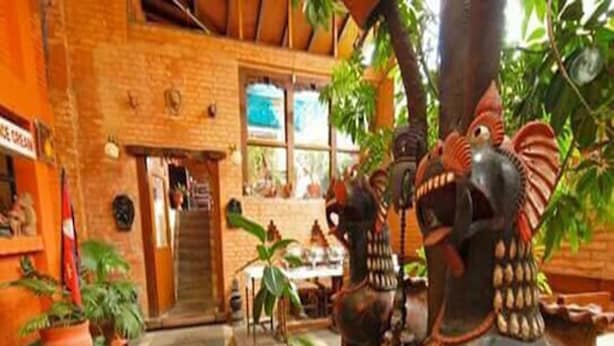 A rustic building with a brick facade, a wooden staircase, and a dining area with a table and chairs. - Cafe de Patan (Lalitpur)