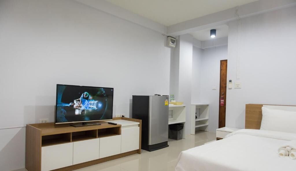 A hotel room with a TV, a minibar, a bed, and a wooden headboard.