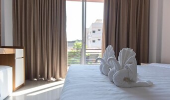 Habitación de hotel con una cama bien hecha, cortinas y vistas a edificios.