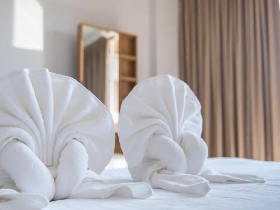 Two neatly folded towels on a bed with a wooden headboard and a mirror in the background.