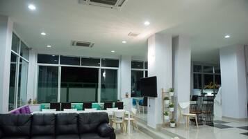 A modern office space with a black leather sofa, a conference table with chairs, a TV mounted on the wall, and large windows.