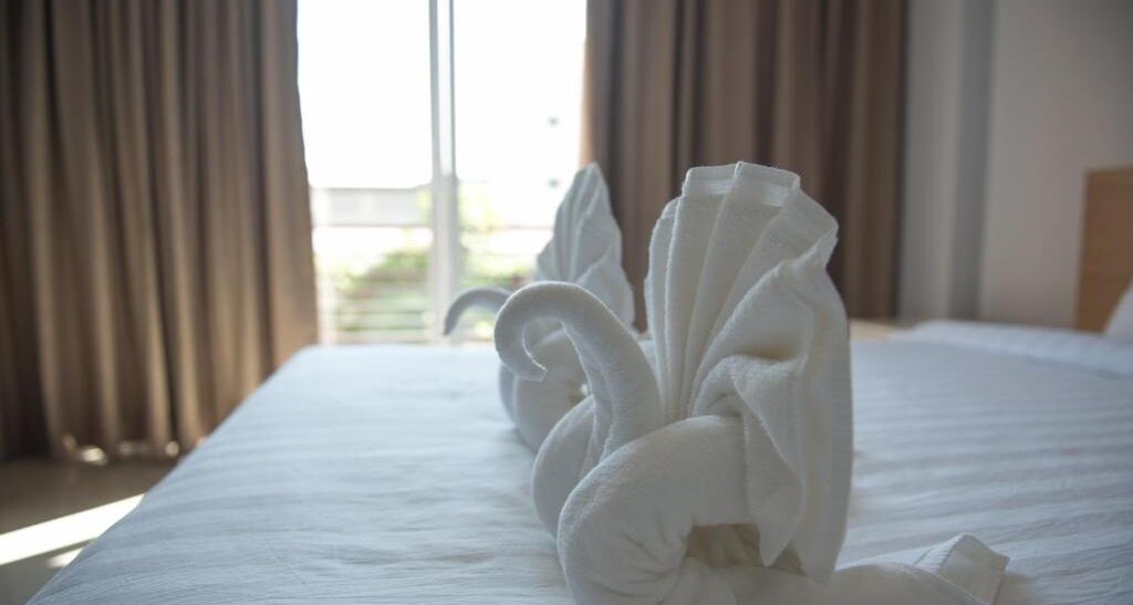 A neatly made bed with a towel arranged in a swan shape.