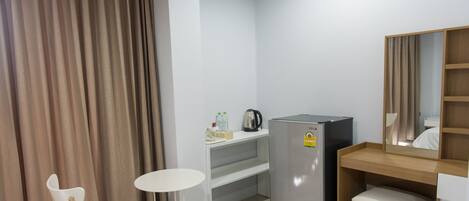 A compact hotel room with a kitchenette, a small table, a chair, and a mirror.
