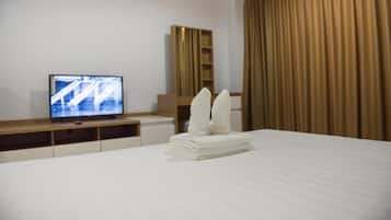 Quarto de hotel com cama bem arrumada, televisão sobre suporte de madeira e uma janela grande com cortinas.
