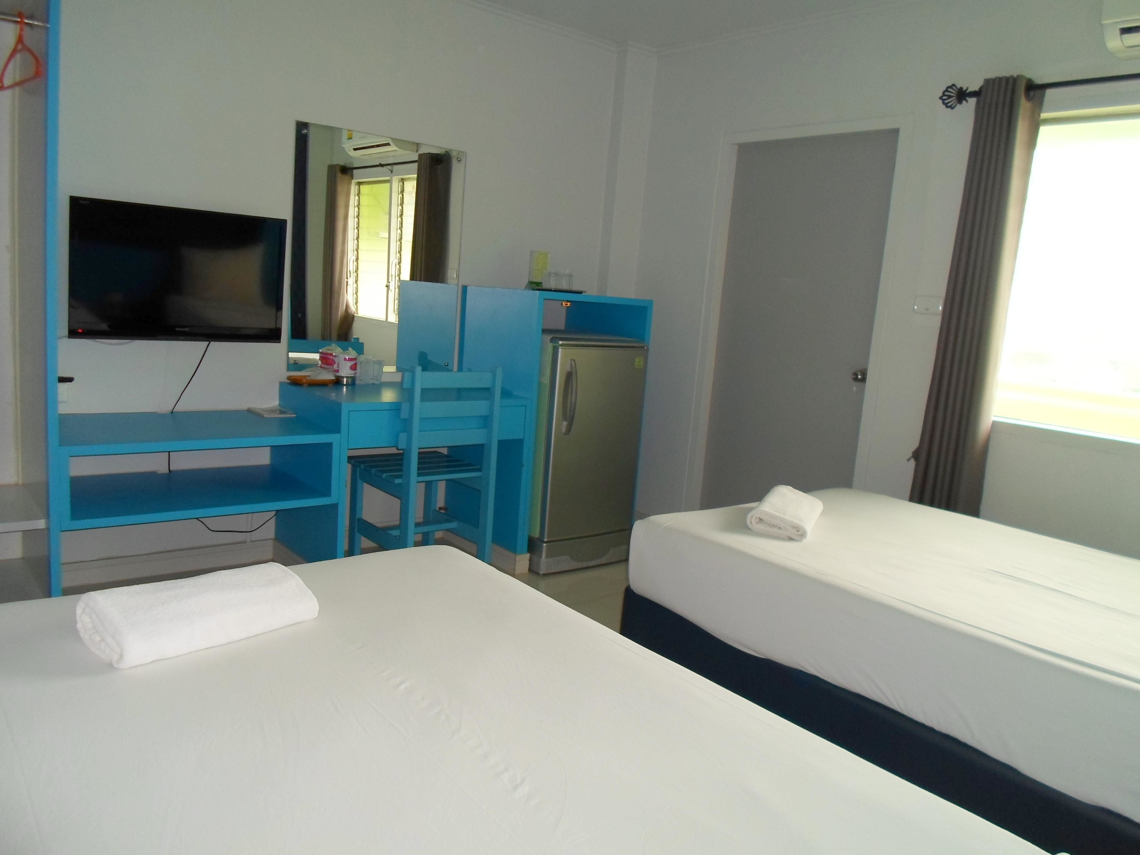 Une chambre d’hôtel comprenant un lit, un bureau avec une chaise, une télévision, un réfrigérateur et une fenêtre avec des rideaux.