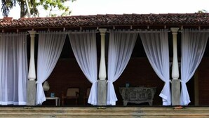 A covered outdoor area with white curtains, a stone bench, and a decorative table. - Arunalu Lake Front (Koggala)
