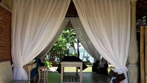 A covered outdoor seating area with a bench and chairs, surrounded by white curtains. - Arunalu Lake Front (Koggala)