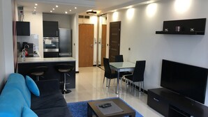 A modern living room with a sofa, a coffee table, a TV, and a dining area with chairs and a table. - JAB Apartments Panoramika i Bandurskiego (Szczecin)