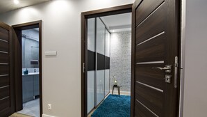 A modern room with a wooden door, a blue carpet, and a glass partition leading to a bathroom. - JAB Apartments Panoramika i Bandurskiego (Szczecin)