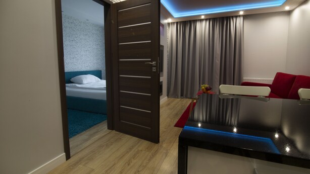 A modern hotel room with a wooden floor, a bed with white linens, a red sofa, and a TV. - JAB Apartments Panoramika i Bandurskiego (Szczecin)
