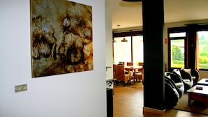 Un interior moderno con un cuadro abstracto grande en la pared, un comedor con mesa y sillas, y vistas a la vegetación a través de las ventanas.