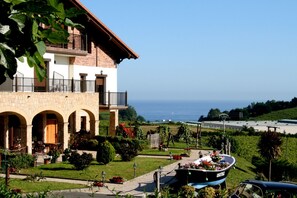 A two-story building with a balcony, a garden with a boat, and a view of the sea. - Usotegi  Agroturismo (Getaria)