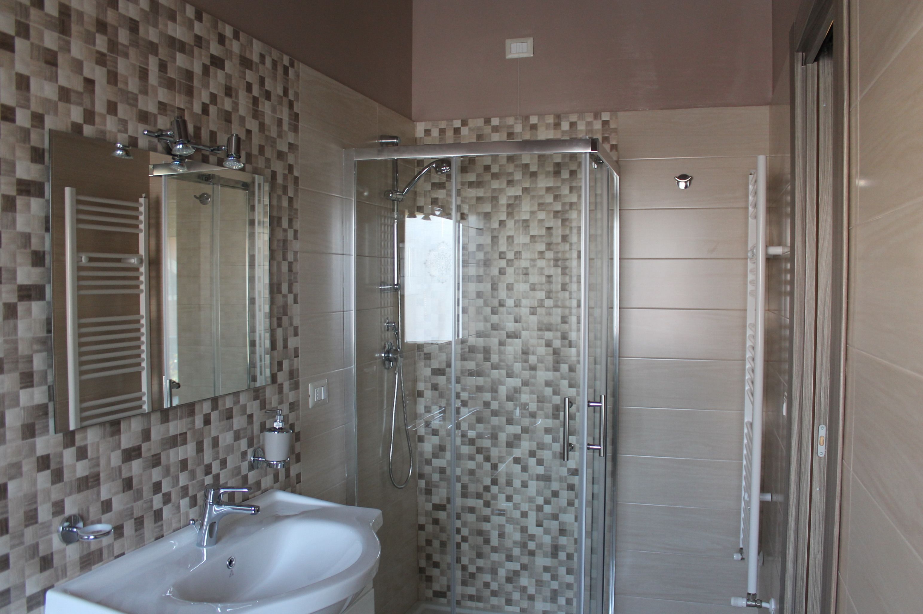 Bagno con doccia vetro, lavandino e specchio.