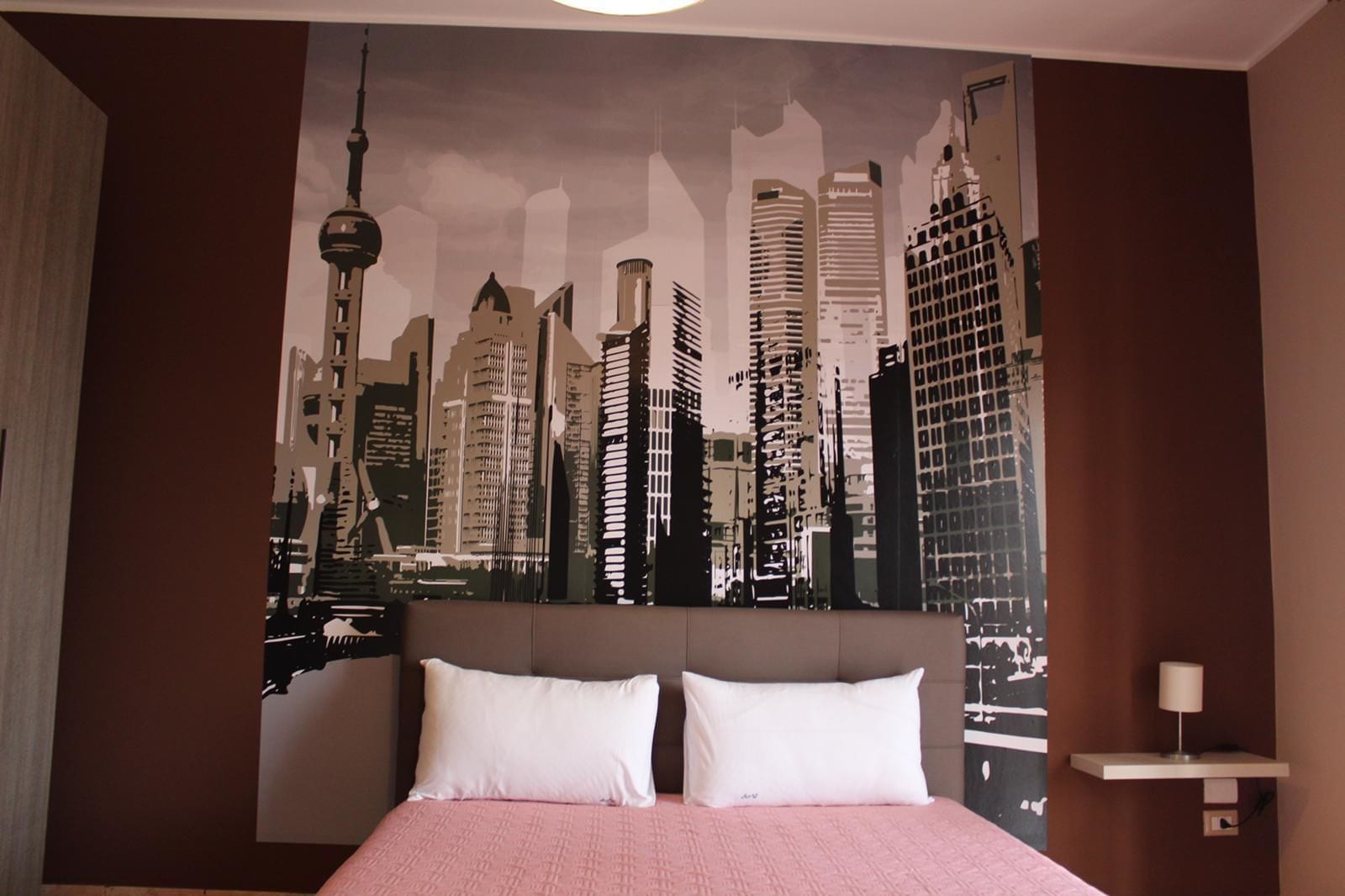 Un dormitorio con una cama grande, dos almohadas blancas y un mural con vistas a la ciudad.