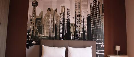 Un dormitorio con una cama grande, dos almohadas blancas y un mural con vistas a la ciudad.