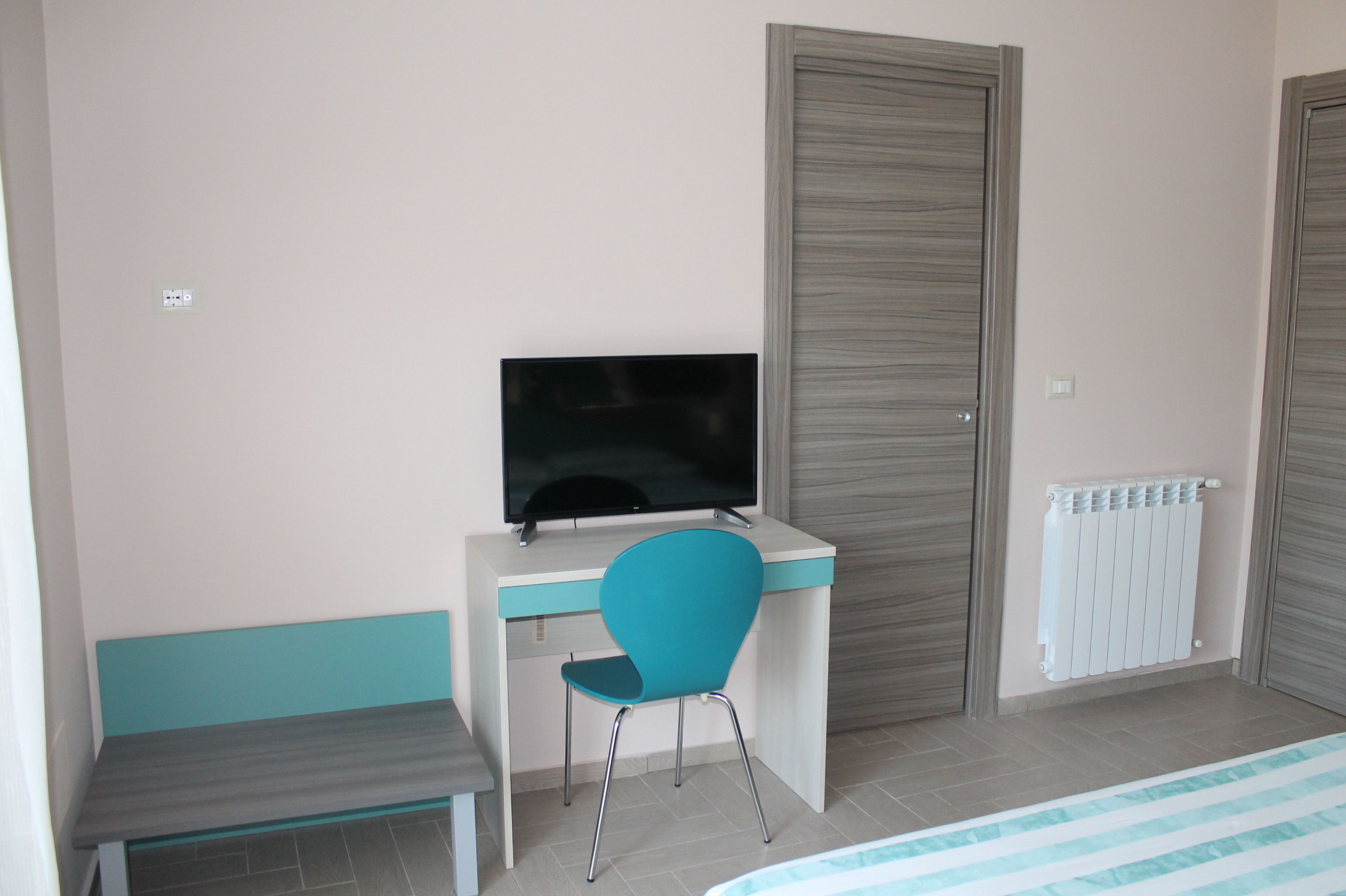 A bedroom with a bed, a desk with a chair, a television, and a radiator.