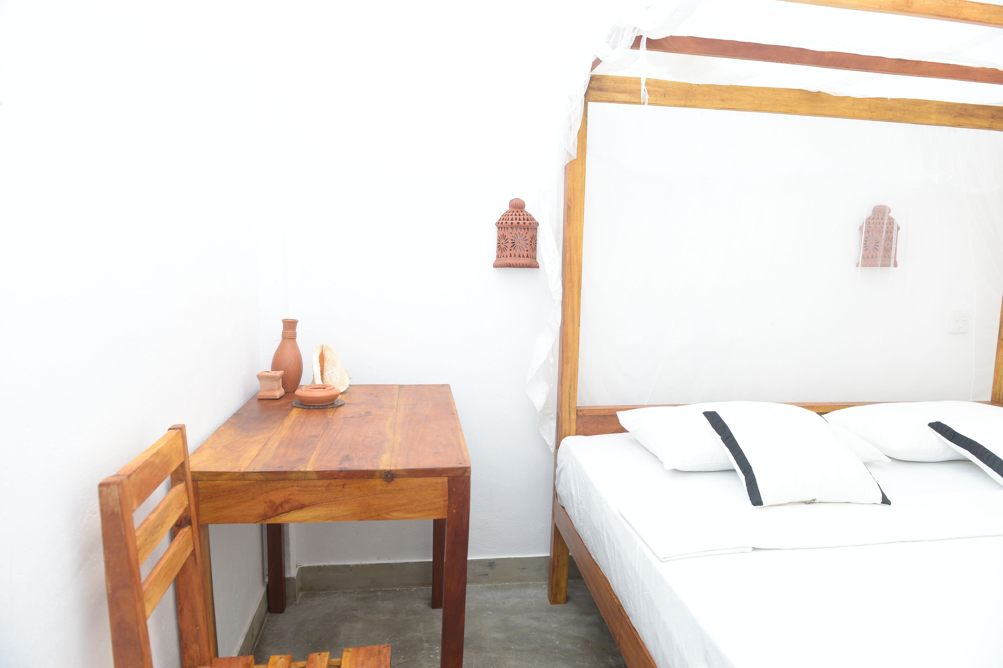 A bedroom with a wooden bed, white bedding, a wooden table with a vase, and two wall-mounted lanterns.