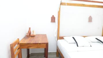 A bedroom with a wooden bed, white bedding, a wooden table with a vase, and two wall-mounted lanterns.