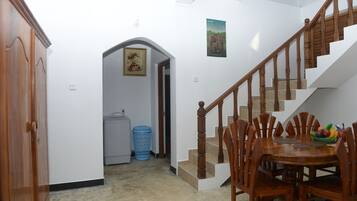 A dining area with a wooden table and chairs, a staircase, and a laundry basket in the background.